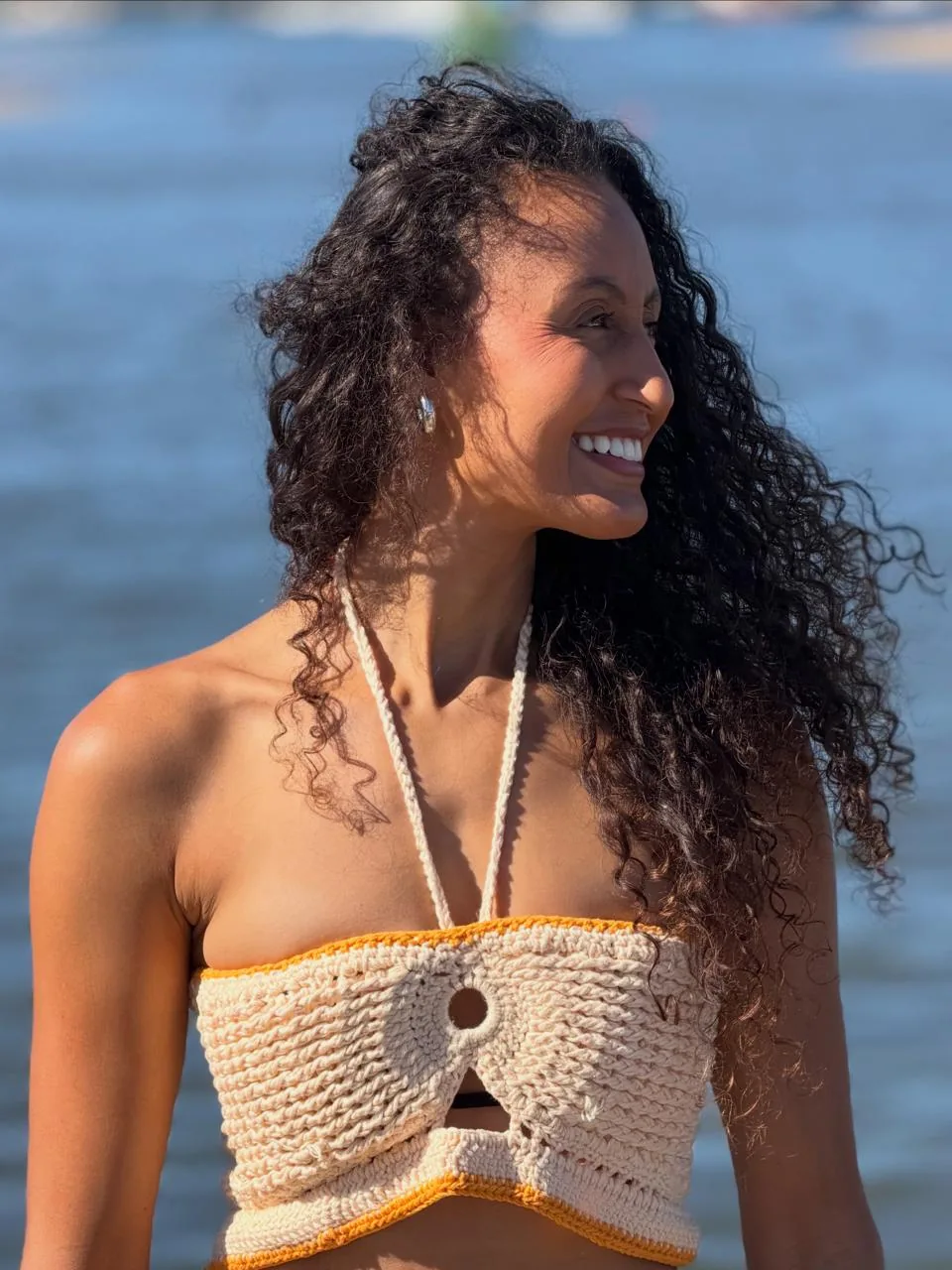 Joelma Marques sorrindo à beira de um lago, ao sol