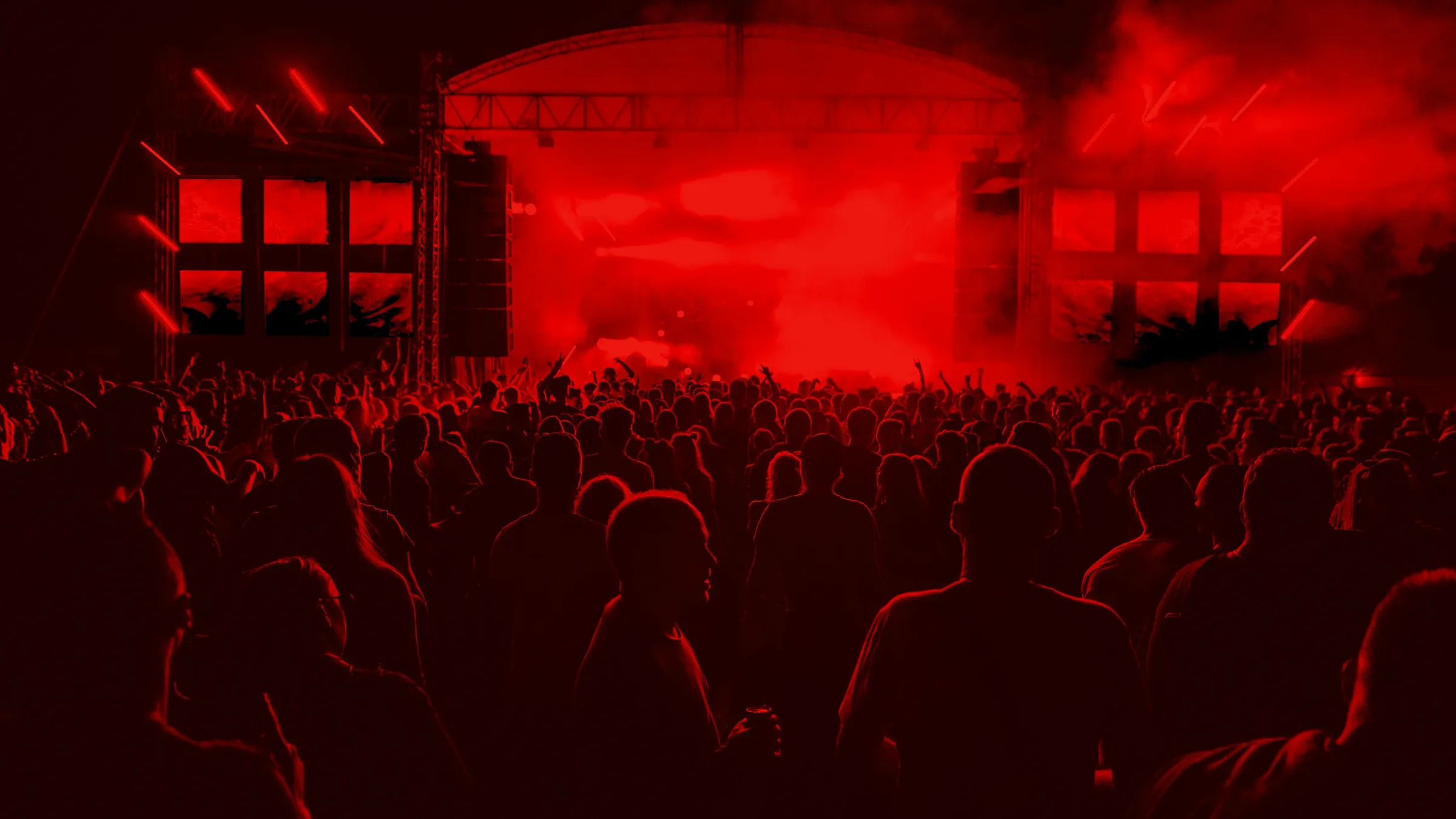 Público de braços levantados diante de um palco iluminado em festival noturno